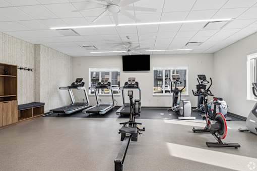 A spacious gym with treadmills, elliptical machines, and a fan.
