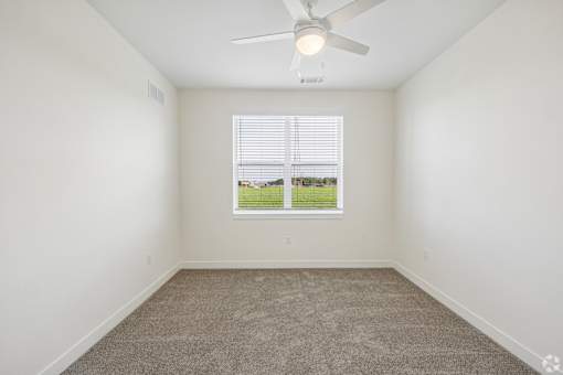 A room with a ceiling fan and a window overlooking a green field.