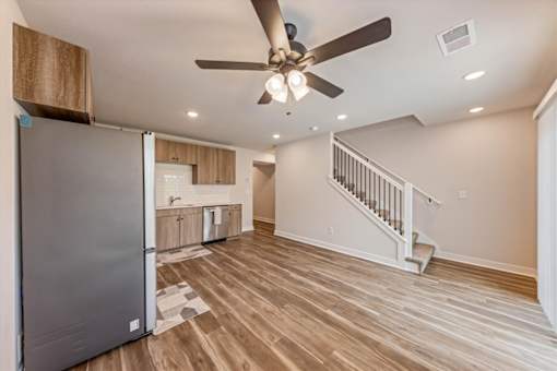 A modern kitchen with a refrigerator, wooden floors, and a ceiling fan.