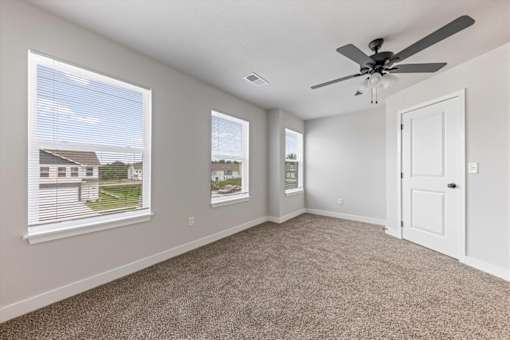 A room with a ceiling fan and two windows showing a view of a house.