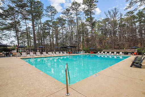 A large swimming pool surrounded by trees and lounge chairs.