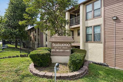A sign in front of a building that says "Tealwood on The Creek Meadow Lane".