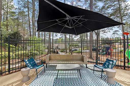 A black umbrella shades a patio with a couch, chairs, and a table.