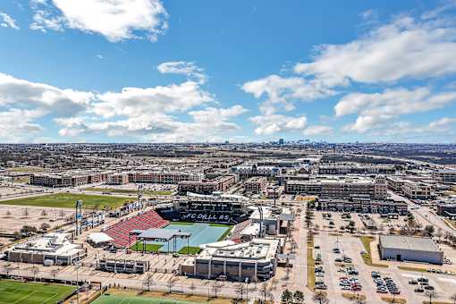 A view of a stadium with a soccer field and a parking lot.
