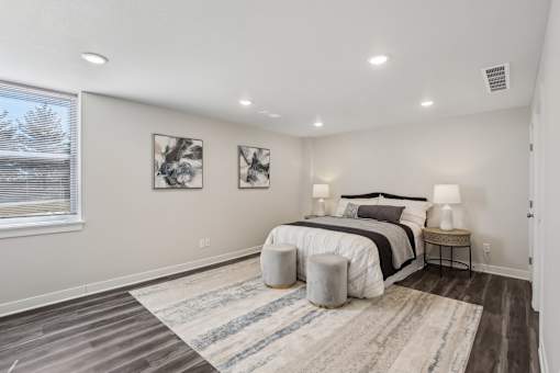 Blue Springs, MO Townhomes - Chapman Ridge Townhomes - A Bedroom With Queen-Sized Bed, Abstract Wall Art, Vinyl Plank Flooring, Matching Bedside Lamps, And A Large Window.