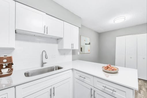 A white kitchen with a sink and a bowl of fruit on the counter.