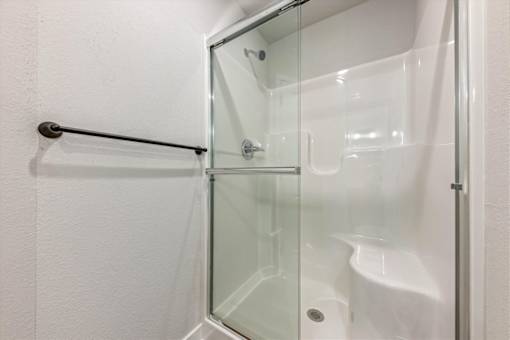 A white shower stall with a glass door and a black grab bar.