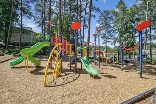 A playground with a yellow and green slide, red and blue climbing structures, and a brown ground.