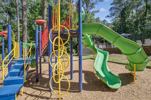 A playground with a green slide and a red umbrella.