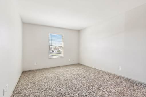 A room with a carpeted floor and a window with blinds.