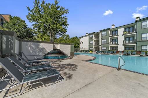 A pool area with sun loungers and a building in the background.
