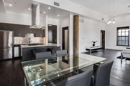 A modern kitchen with a glass table and grey chairs.