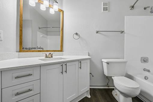 A white bathroom with a gold framed mirror and a towel rack on the wall.