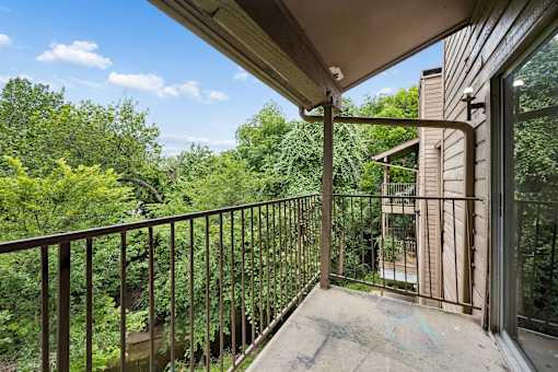 A balcony with a metal railing overlooks a wooded area.