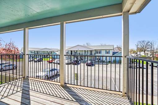 A view from a covered walkway looking out to a parking lot and buildings.