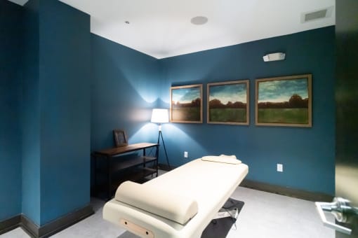 2-Bedroom Apartments in
Germantown, Nashville, TN -
Peyton Stakes - Massage Room
with Blue Walls, White Massage
Bed, Side Table with Shelves,
Standing Lamp, and Wall Art.