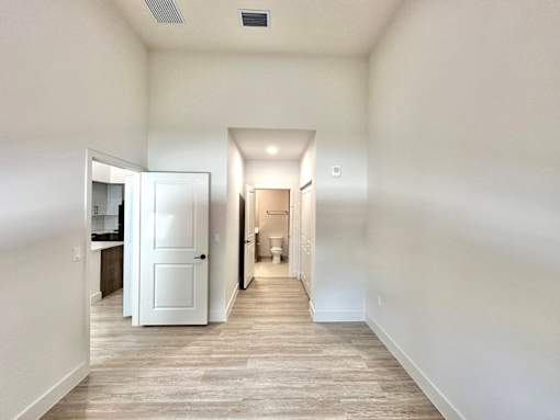 A long hallway with a white door on the left and a toilet in the distance.