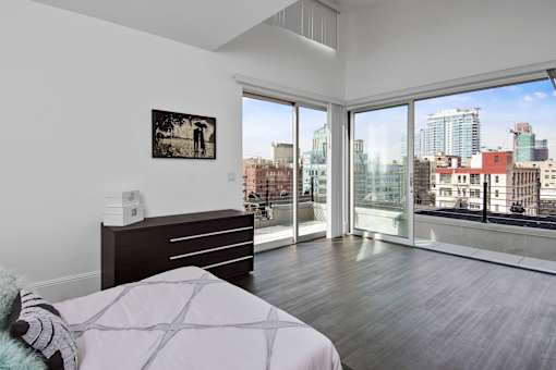 A bedroom with a large bed and a city view through the windows.
