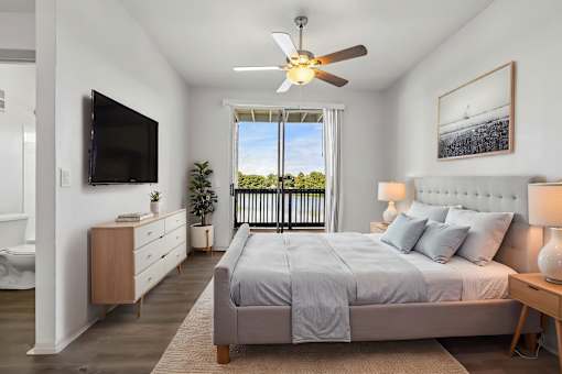A bedroom with a large bed, a flat screen TV, and a balcony with a view of trees.