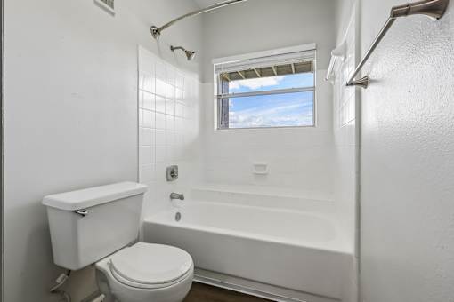 A white bathroom with a toilet, tub, and window.
