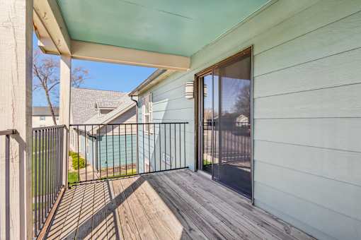 A wooden deck with a metal railing and a sliding glass door leading to a pool.