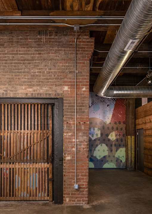 A large metal pipe runs along the ceiling of a room with a brick wall and a wooden gate.