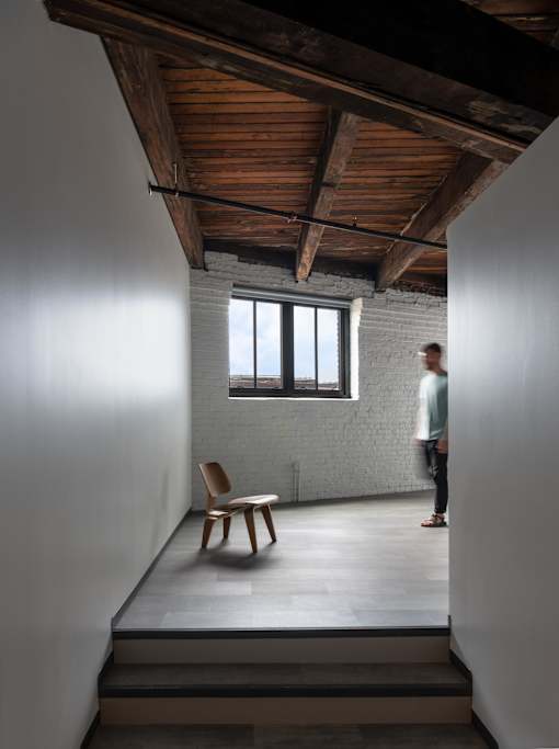 A man stands in a room with a wooden chair and a window.