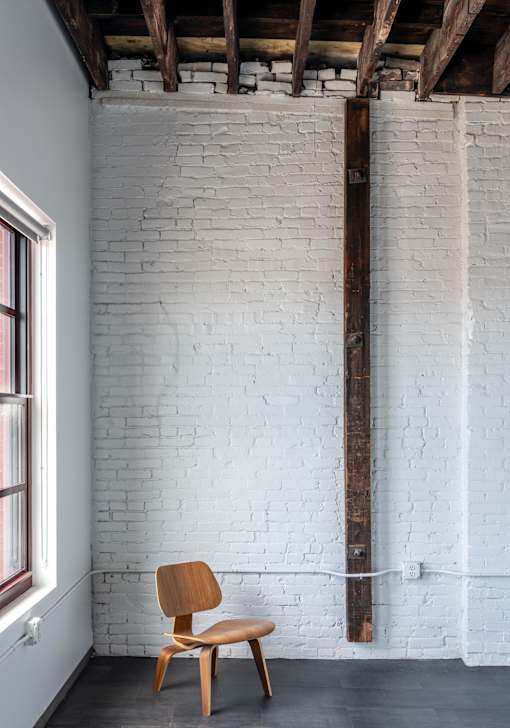 A wooden chair sits in front of a white brick wall.