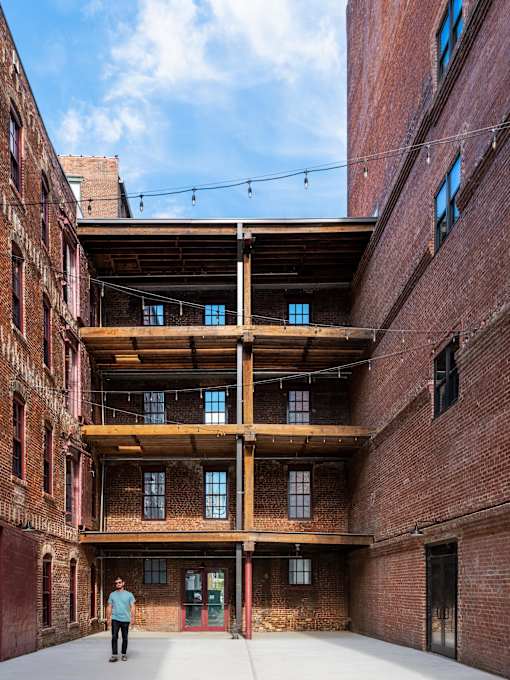 A man stands in a large, open atrium between two brick buildings.