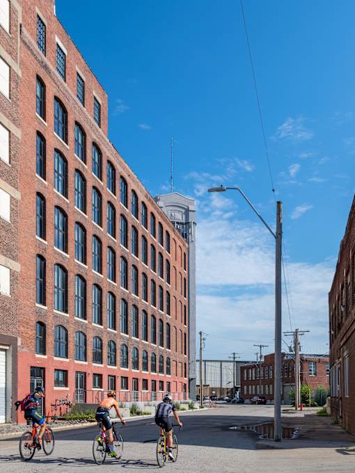 Three people riding bikes in front of a red brick building.