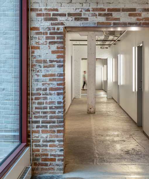 A person walks down a hallway with brick walls and concrete floors.