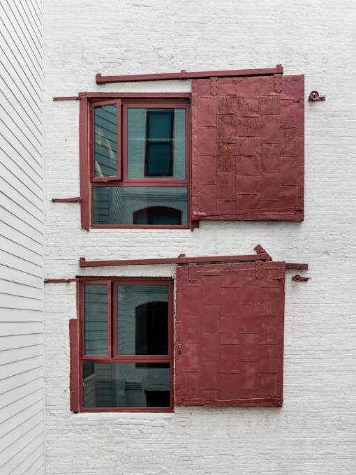 Two windows with red shutters on a white building.