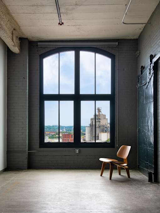 A chair sits in front of a large window in a room with exposed brick walls.