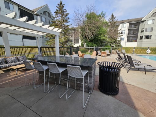 a patio with a table and chairs and a trash can in front of a pool