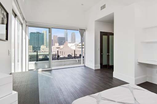 A large white bed sits in a room with a view of the city.
