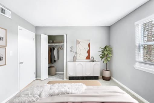 A white bedroom with a bed, a wardrobe, and a plant.