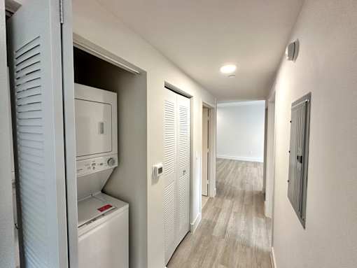 A white washing machine is in a small room with a door open to a hallway.