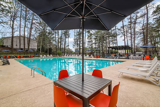 A pool area with a table and chairs under an umbrella.