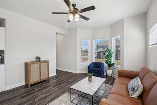 A living room with a brown leather couch, a wooden cabinet, a blue chair, and a ceiling fan.