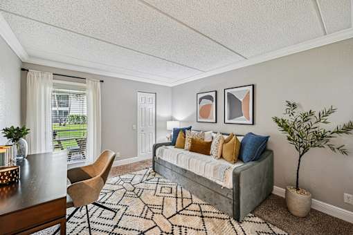 A living room with a grey couch, a wooden table, a rug and a potted plant.
