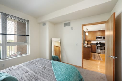 a bedroom with a large window and a door to a kitchen at Verge Apartments in St. Louis Park, MN