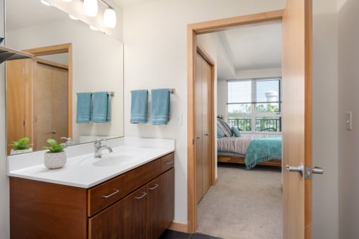 a bathroom with a mirror and a sink and a door to a bedroom at Verge Apartments in St. Louis Park, MN
