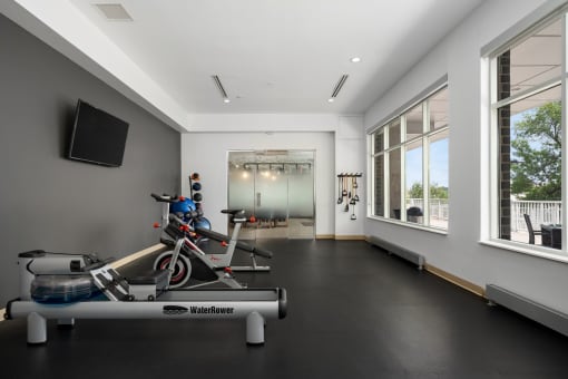 a workout room with a bike and other exercise equipment in a building with large windows at Verge Apartments in St. Louis Park, MN