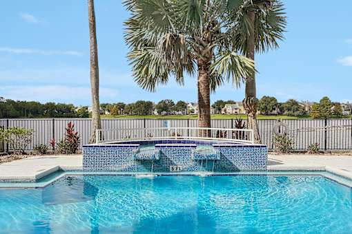 A pool surrounded by palm trees and a fence.