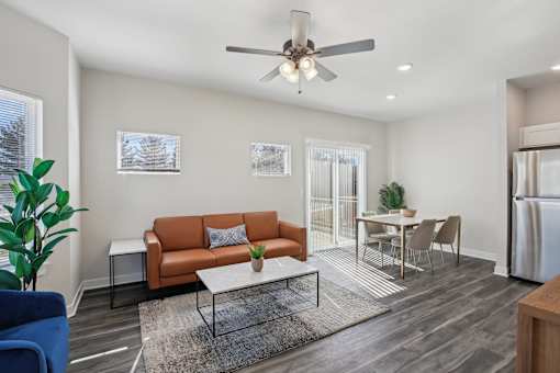Four Bedroom Townhomes In Blue Springs, MO - Chapman Ridge Townhomes - A Living Room With Tan Leather Sofa, Large Window, Glass Sliding Doors, Ceiling Fan, And A Sleek Table.