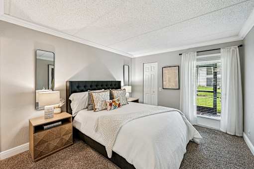 A bedroom with a large bed and a window with white curtains.