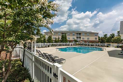 A pool surrounded by a white fence with trees in the foreground.