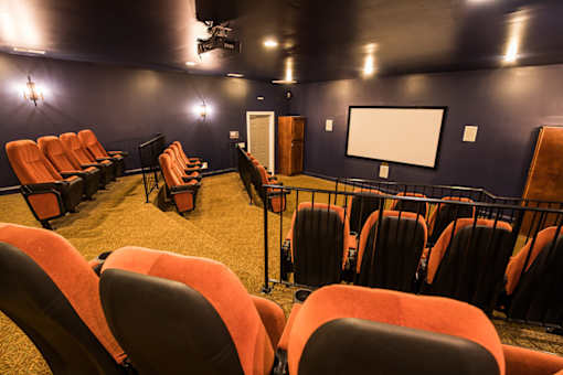 A row of orange chairs are arranged in front of a screen in a dark room.