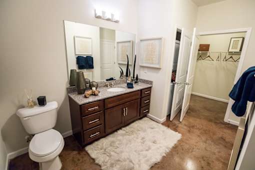 A bathroom with a white toilet, a sink with a brown counter, and a white rug.