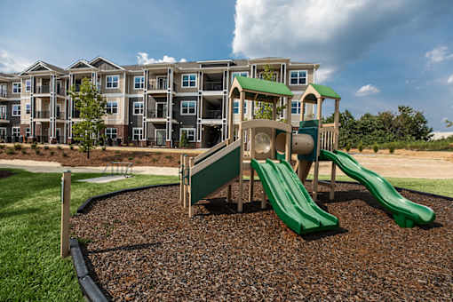A playground with a green slide in front of apartment buildings.